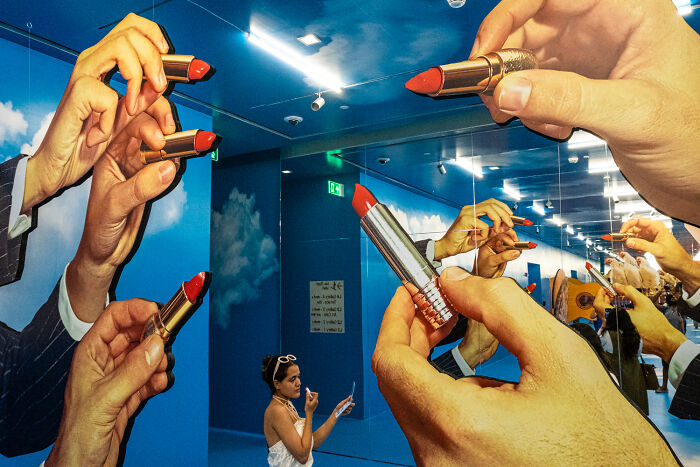 Woman posing inside an art installation with large hands holding red lipstick, showcasing unforgettable street photos.