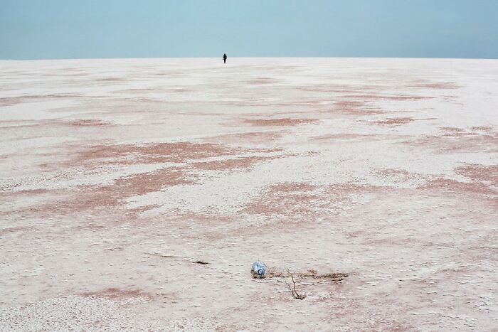 Lone person walking across vast barren land with textured salt flats, showcasing nature and life around the world.