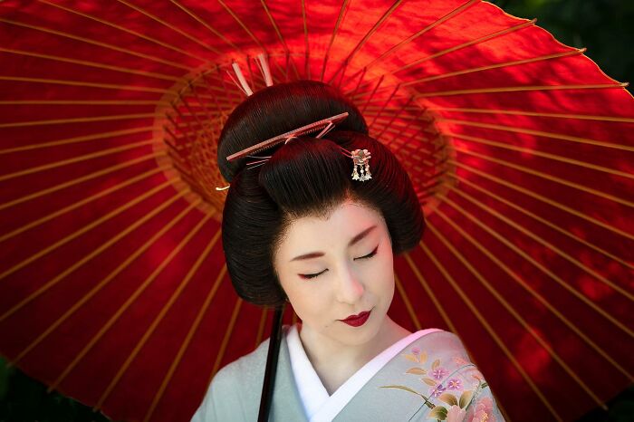 Woman in traditional Japanese attire holding a red umbrella, showcasing stunning photos capturing people and life around the world.