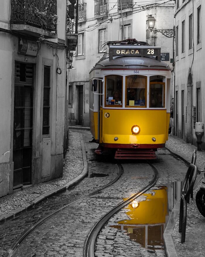Yellow tram traveling through narrow cobblestone street with tracks and reflections, capturing stunning life around the world.