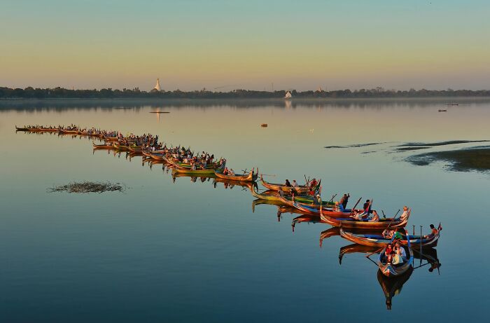 Long row of colorful boats with people rowing on calm water, capturing stunning nature and life around the world.