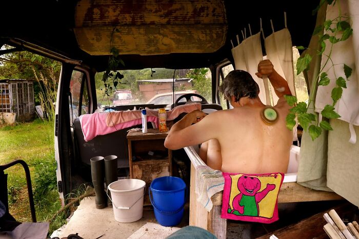 Man bathing inside a rustic vehicle surrounded by nature, capturing stunning photos of people and life around the world.