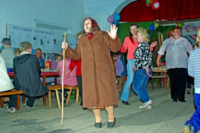 Elderly woman dancing with a stick among people at an indoor social gathering, capturing life and people around the world.