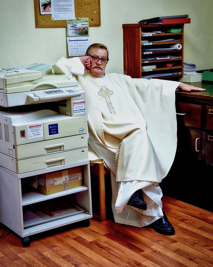 Older man in clerical robes sitting beside office equipment, capturing nature, people, and life around the world in an indoor setting.
