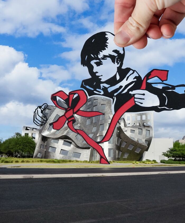 Hand holding paper cutout of a boy tying a red ribbon around a modern building in a creative travel art scene.