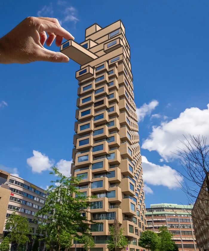 Hand holding paper cutout positioned to extend a modern high-rise building in a creative artist travels the world scene.