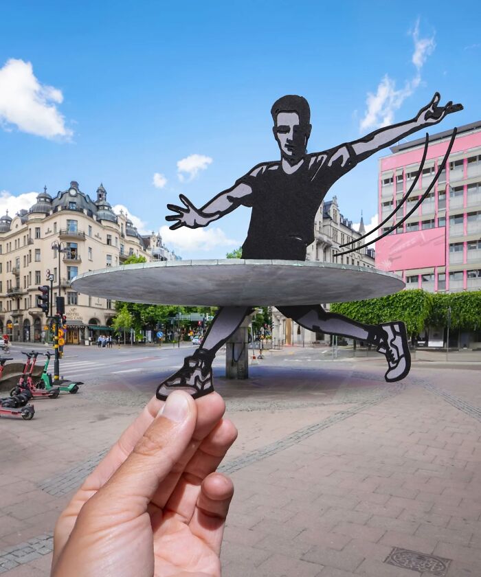 Hand holding paper cutout of a dancer creating a surprising scene in a city, showcasing artist travels and creativity.
