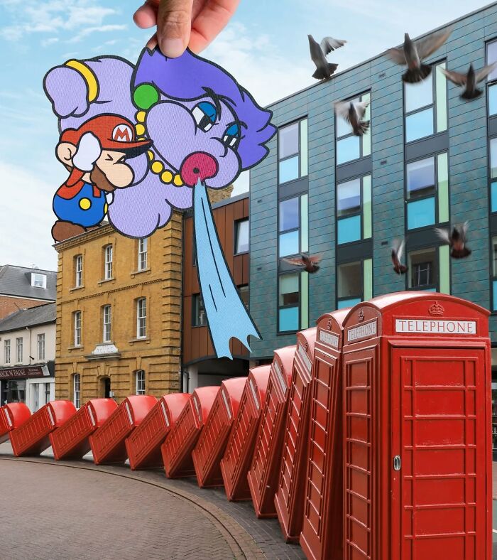 Hand holding paper cutouts of Mario and a purple face cartoon over a street with red telephone booths in a creative artist scene.
