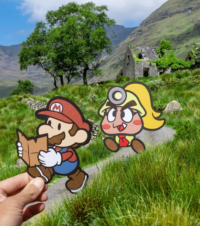 Hand holding paper cutouts of cartoon characters in a scenic landscape, showcasing artist travels and creative scenes.