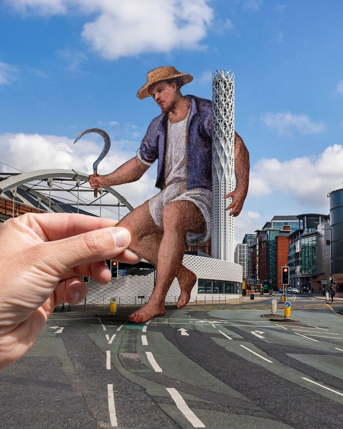 Hand holding a paper cutout of a giant farmer in a city street, showcasing artist travels the world with paper cutouts.
