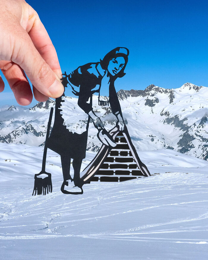 Hand holding paper cutout of a woman sweeping snow on mountain slopes, creative art scene using paper cutouts.