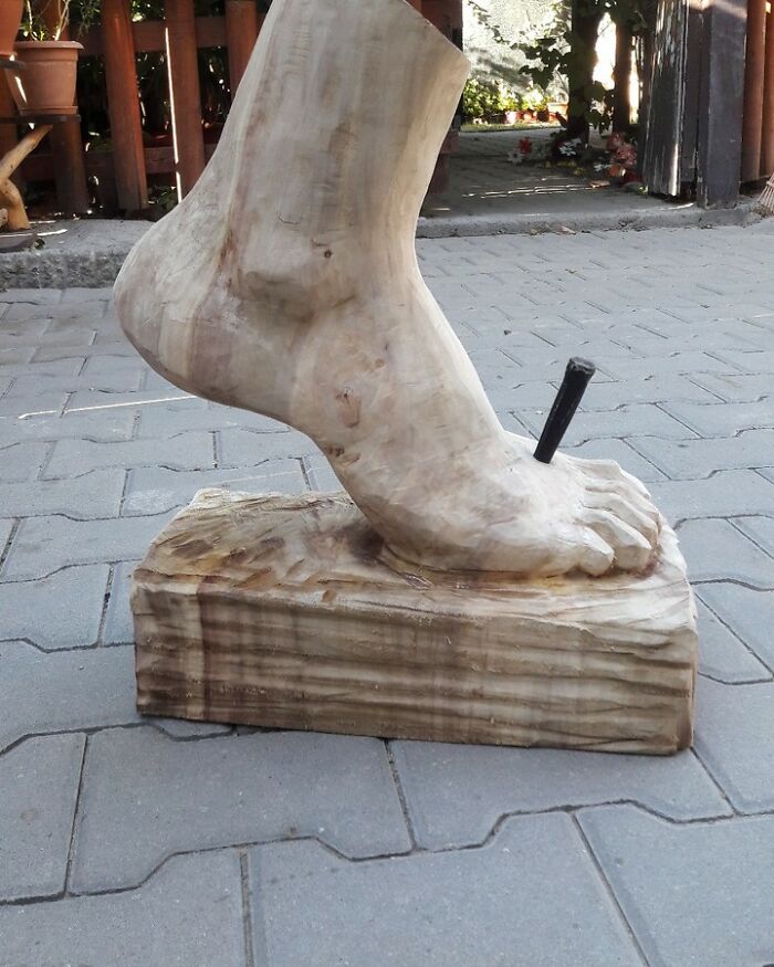 Wooden sculpture of a foot with a nail, an example of chainsaw artist transforming forgotten trees into art outdoors.
