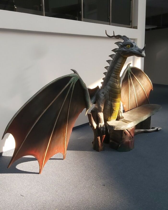 Chainsaw artist's detailed dragon sculpture bench carved from a forgotten tree, showcasing intricate wings and lifelike features.