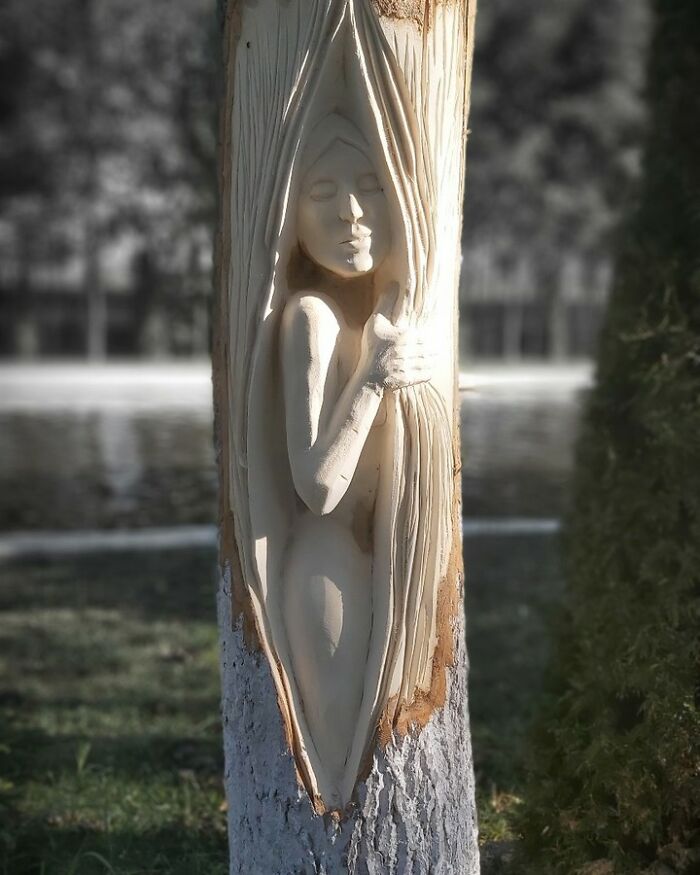 Chainsaw artist carving a detailed female figure emerging from a tree trunk, showcasing transforming forgotten trees into art.
