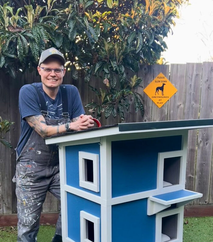 Man smiling beside a custom-built house for a tuxedo cat sleeping on his porch in a backyard setting. Man smiling beside a custom-built house for a tuxedo cat sleeping on his porch in a backyard setting.