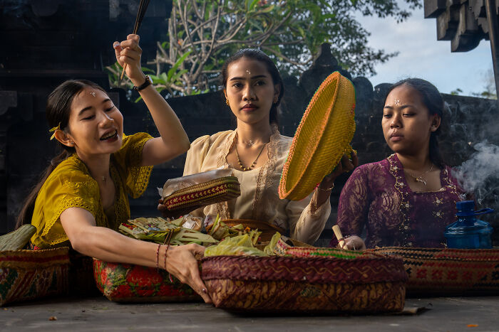 Three women in traditional clothing preparing cultural offerings outdoors, showcasing the beauty of cultures captured by photographer.