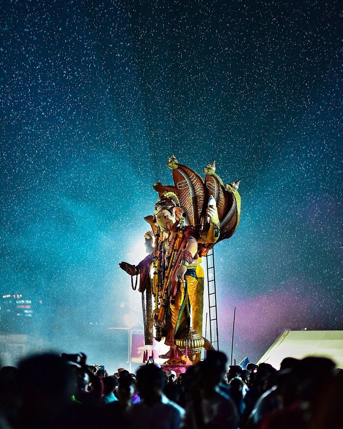 Vivid photo of a colorful Ganesh statue illuminated at night with a crowd celebrating in India during rain.