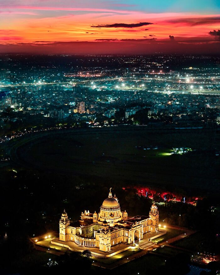 Illuminated historic building at night with city lights and vibrant sunset colors in India cityscape.