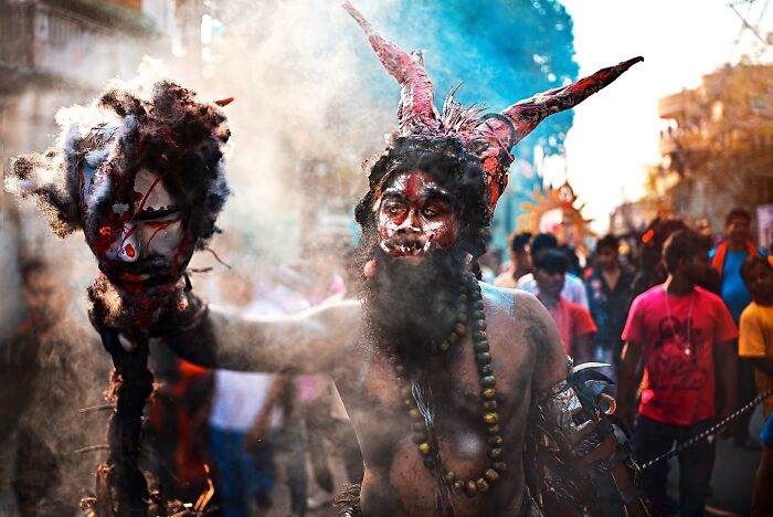 Man in elaborate costume and face paint holding a prop at a vibrant cultural festival in India bursting with color and life.