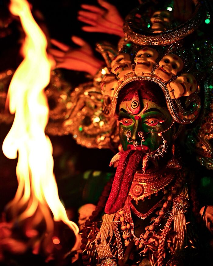 Vivid photo of an Indian performer in colorful traditional makeup and costume with a fiery flame in the foreground.