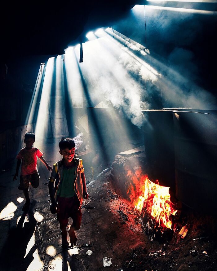 Two children walking near a fiery hearth with vivid sunlight and smoke illuminating the vibrant scene in India.
