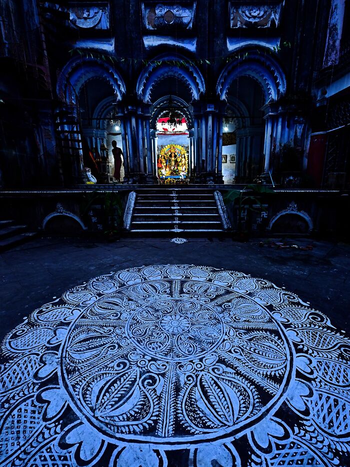 Intricate white rangoli design in front of a traditional Indian temple entrance bursting with color and life.