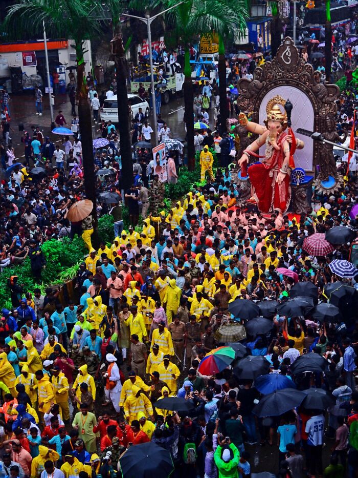 Crowd in vibrant clothing carrying a large colorful statue during a lively street festival in India bursting with color and life.