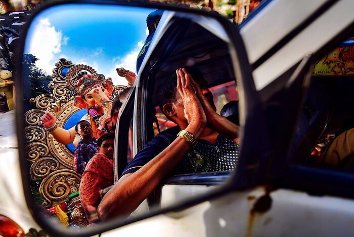 Colorful vivid photo of India showing a man praying reflected in a car mirror with a decorated Ganesha idol in the background