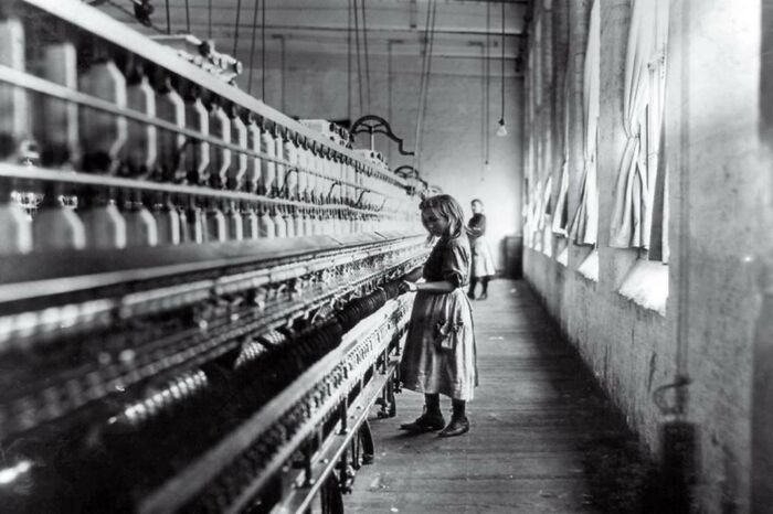 Young girl working at a long cotton spinning machine in a factory, a striking photo capturing iconic moments in history.