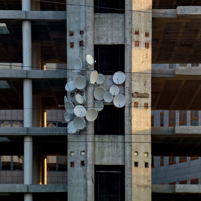 A cluster of satellite dishes arranged as street art on the concrete wall of an unfinished building.