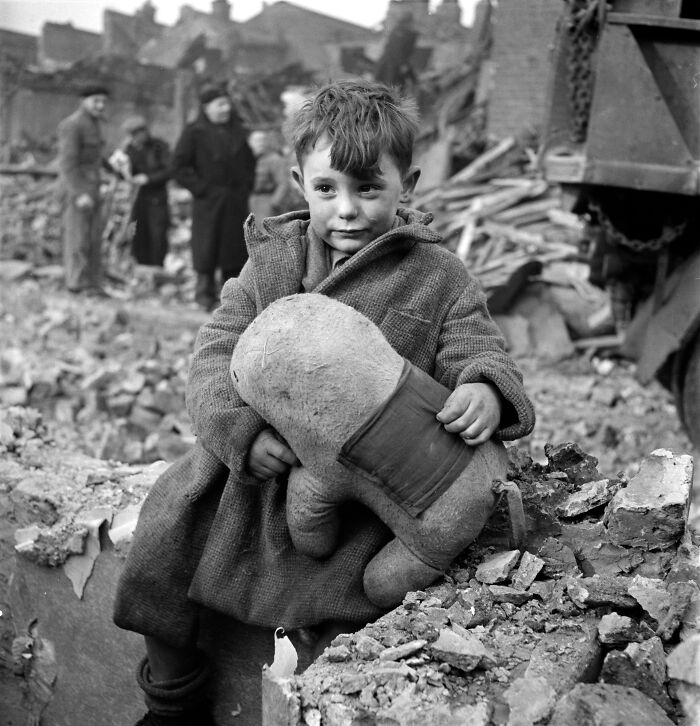 Young boy holding a teddy bear amidst rubble in a striking photo capturing an iconic moment in history.
