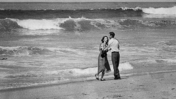 Couple dancing on the beach with ocean waves behind them in a striking photo capturing iconic moments in history.