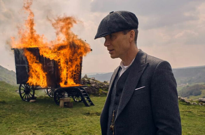 Actor in period costume stands near a burning wagon, illustrating celebs being out-of-touch while trying to be relatable.