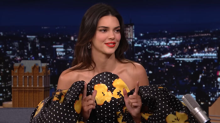 Celebrity wearing a floral off-shoulder dress, showing entitlement while discussing work and life on a late-night talk show.