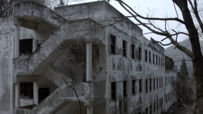 Large abandoned concrete building with peeling paint and bare trees in a gloomy setting, illustrating abandoned places.