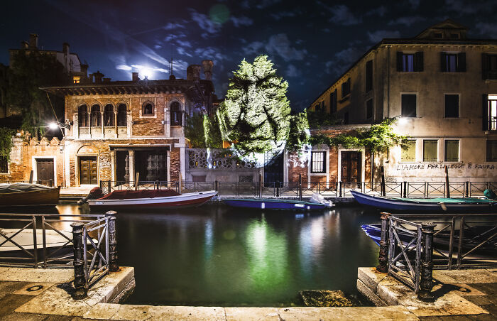 Night scene of street art projection on building facade by a canal with boats, showcasing creative street art photos.