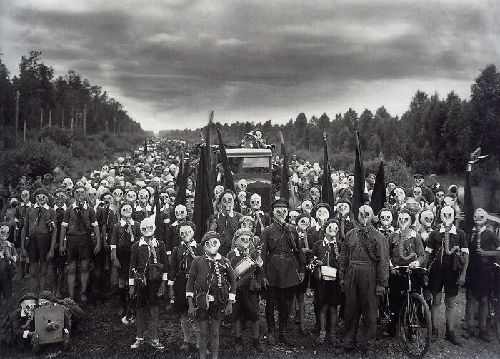Large group of people wearing gas masks in a wooded area, capturing a creepy and unsettling moment in history.