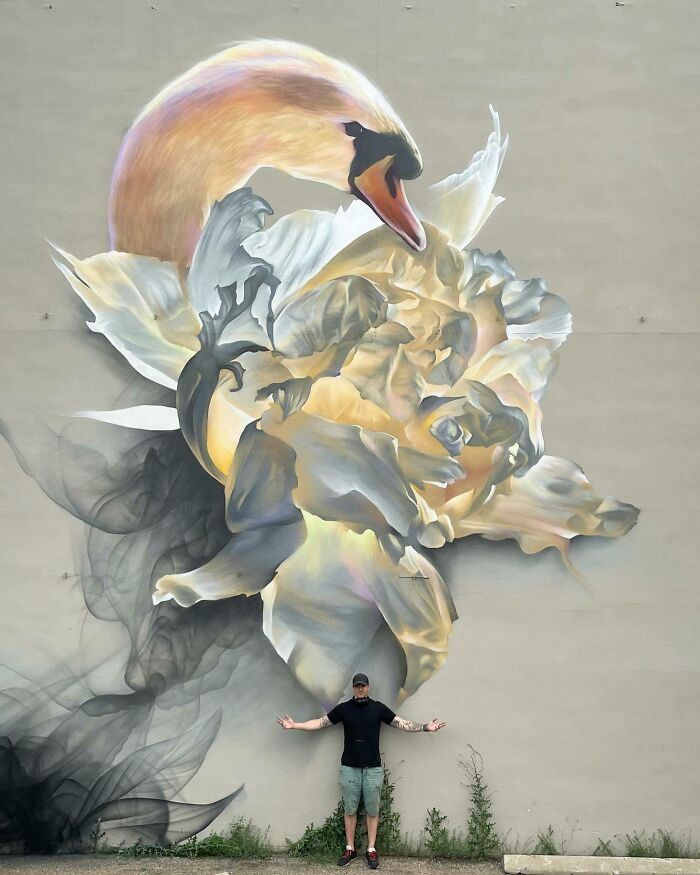 Mural blending graffiti, realism, and abstraction featuring a swan and floral design with artist standing below on pavement.