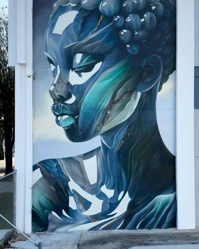 Mural by Alexander Vizsla Bacon featuring a blue-toned female portrait blending graffiti, realism, and abstraction on a building wall.