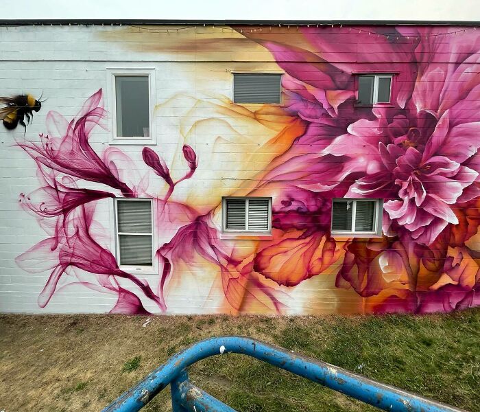 Colorful mural blending graffiti, realism, and abstraction with floral designs and a bee on an urban building wall.