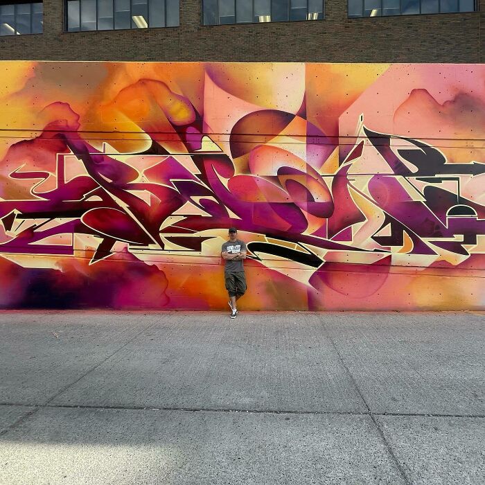 Man standing in front of a vibrant graffiti mural blending realism and abstraction by Alexander Vizsla Bacon.