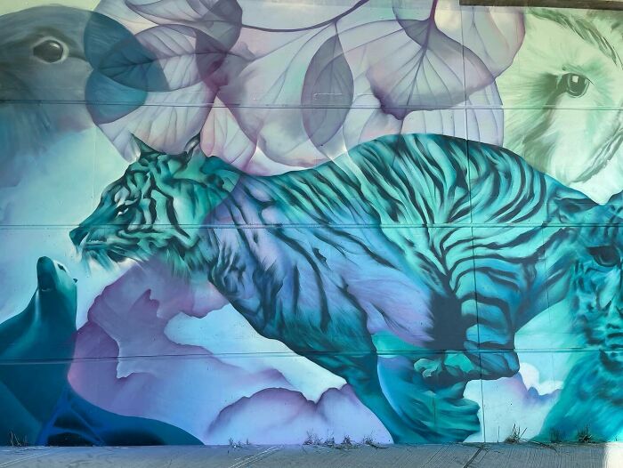 Mural blending graffiti, realism, and abstraction depicting a large blue tiger with abstract shapes and animal faces.