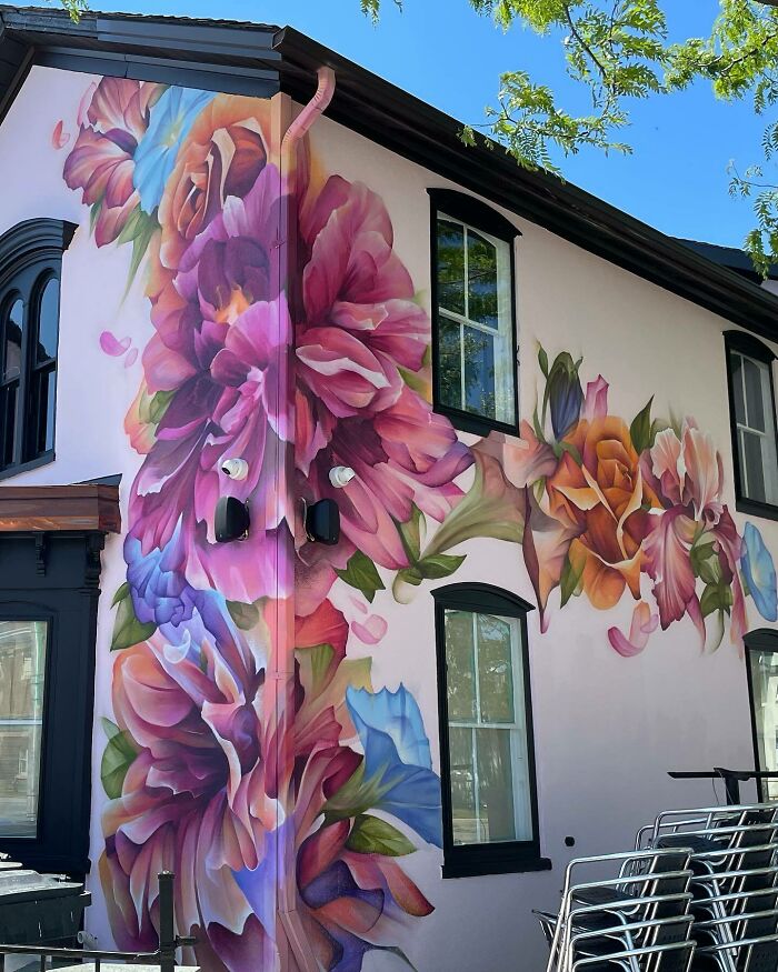 Colorful mural featuring large flowers blending graffiti, realism, and abstraction on the exterior wall of a building.