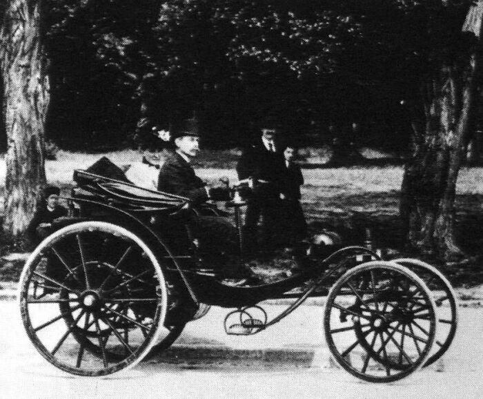 Early 1900s vintage car with large spoked wheels driving on a road, showcasing how wild the first cars really were.