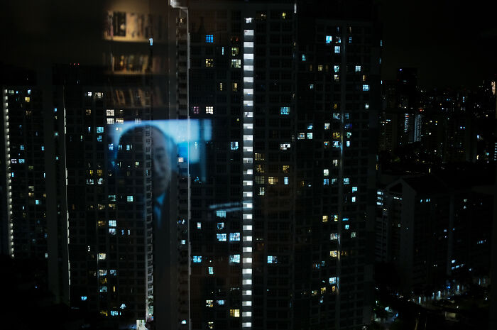 Night cityscape with illuminated windows reflecting a cinematic image, showcasing a photographer’s poetic, cinematic style.