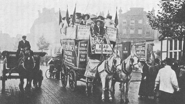 Historic black and white photo of women in the 20th century suffrage era riding a horse-drawn campaigning wagon.