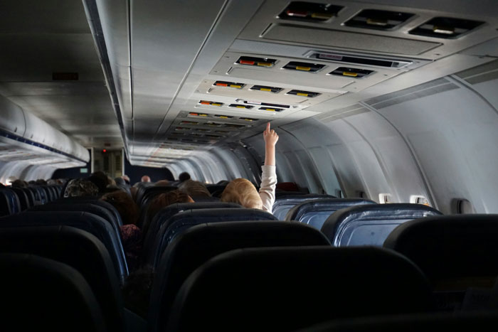 Passenger in airplane cabin raising hand during flight, illustrating extreme diarrhea leading to emergency landing and cancellation.