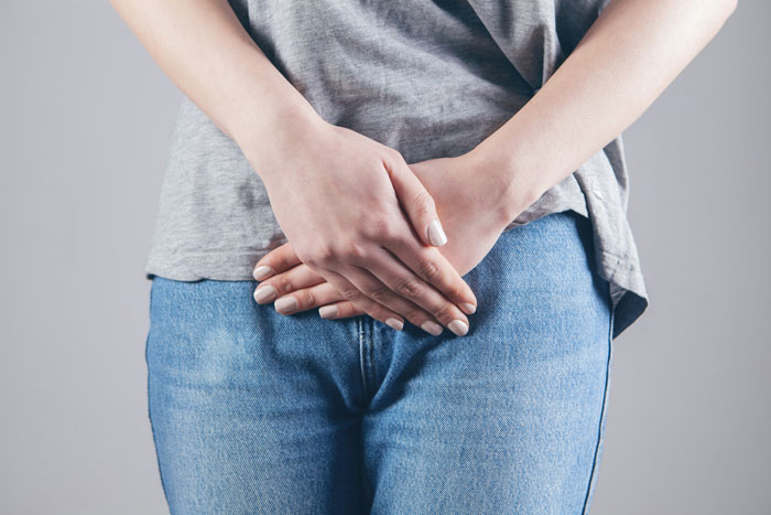 Woman in jeans and gray shirt holding hands over abdomen, depicting extreme diarrhea discomfort on plane.