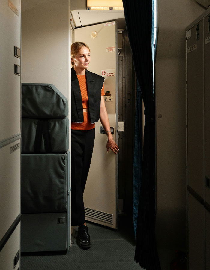 Woman standing near airplane lavatory door, illustrating extreme diarrhea incident causing emergency landing and flight cancellation.