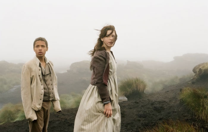 Two actors in period clothing on a foggy moorland setting, from the controversial Wuthering Heights adaptation.